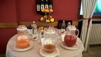 Una mesa de desayuno con tres jarras de bebidas, una presentación de frutas y botellas de vino en la pared.