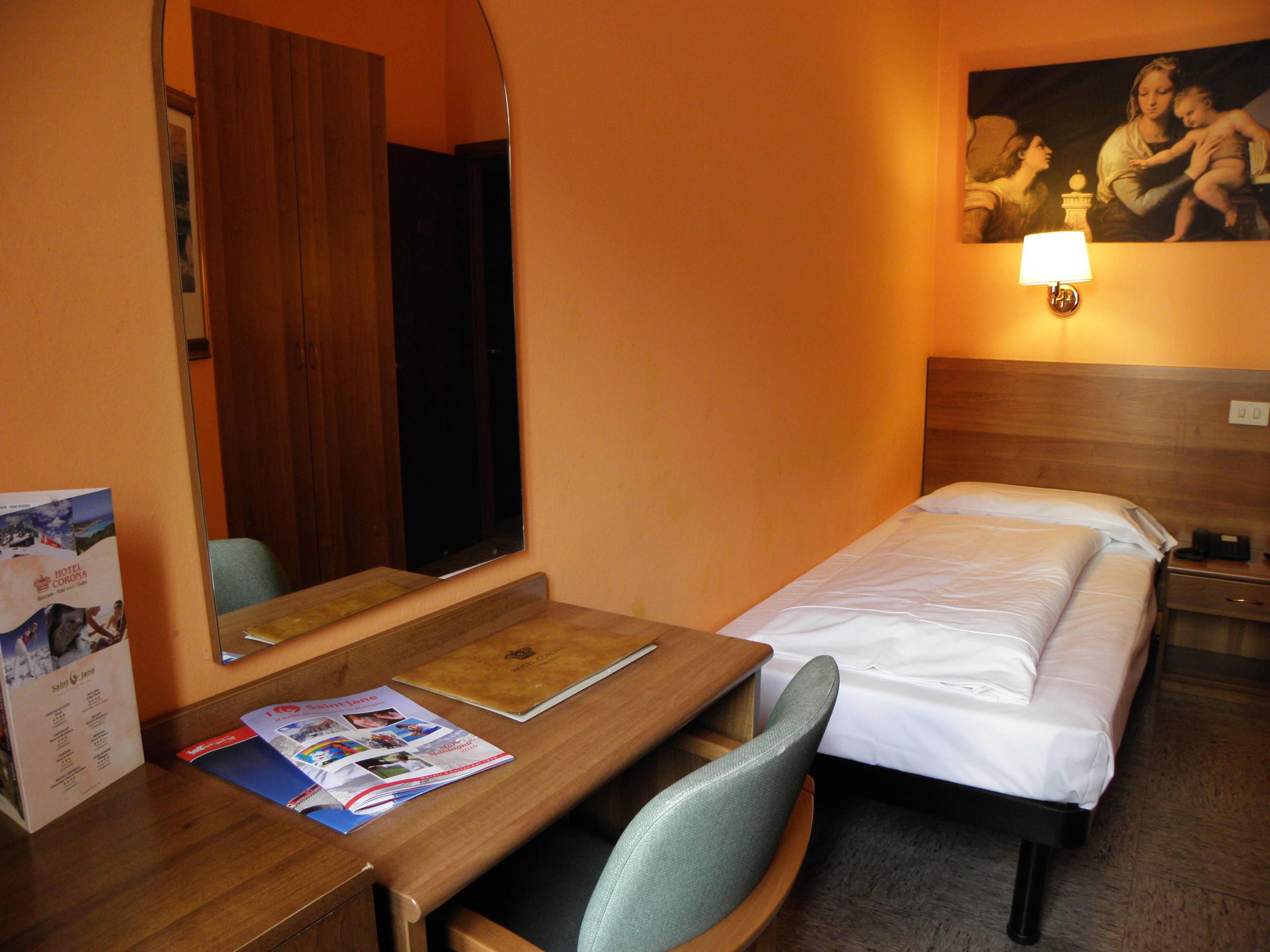 Ein Hotelzimmer mit einem Holztisch, einem Bett mit weißer Bettwäsche, einem Nachttisch, einer Lampe und einem großen Spiegel.