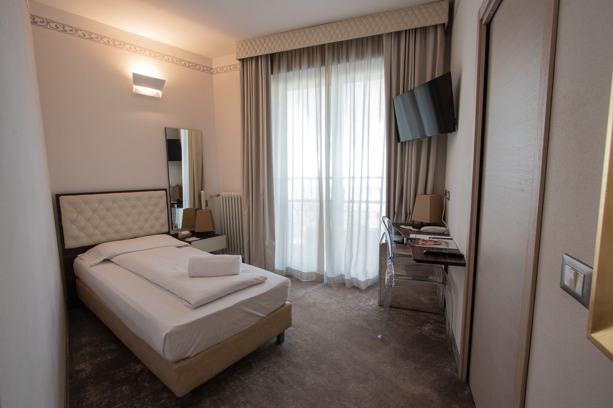 Habitación de hotel con cama, escritorio, silla, televisor y ventana con cortinas.