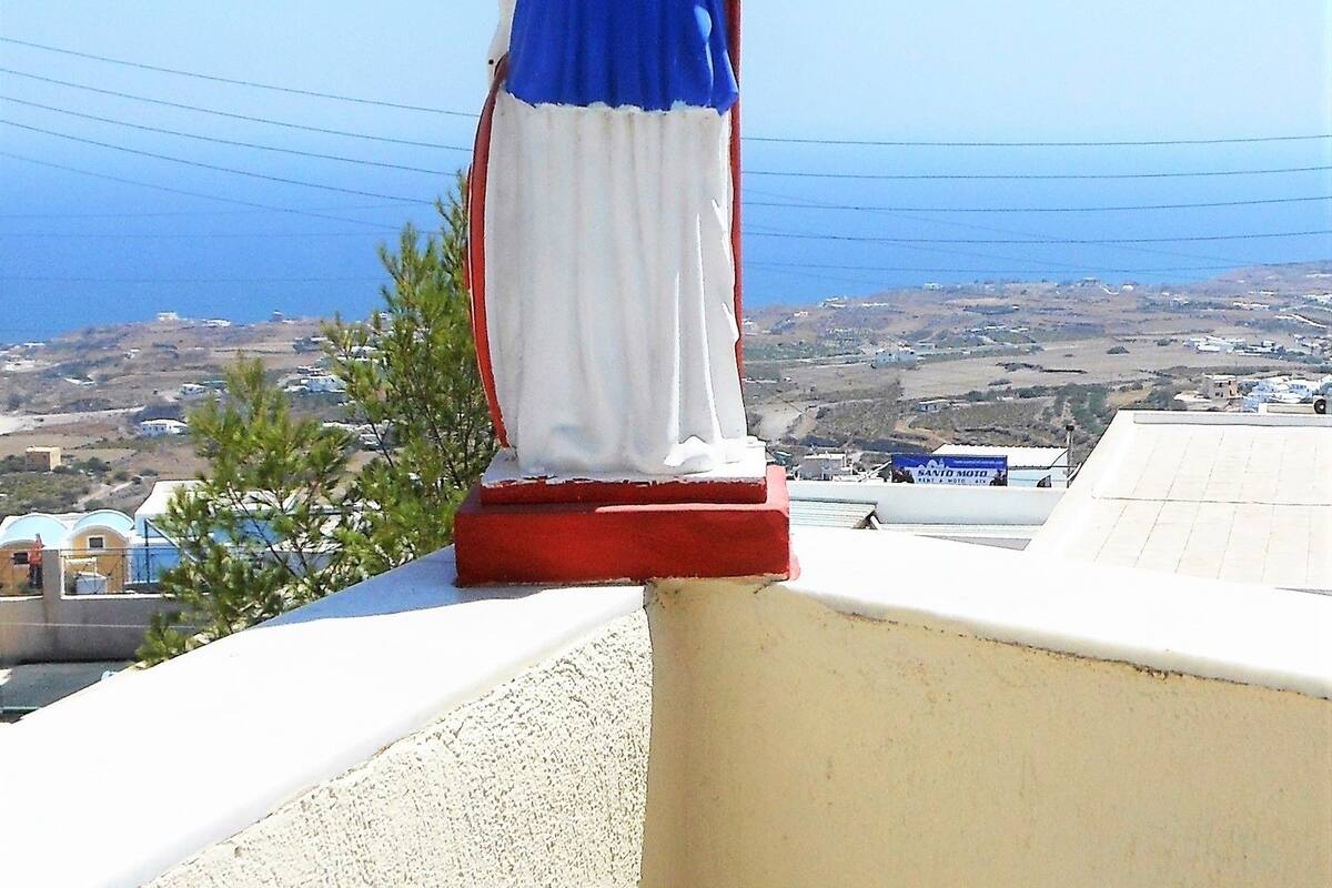 Une statue représentant une figure vêtue d’une robe bleue et d’un chapeau rouge, placée sur un balcon d’où l’on peut admirer la mer.