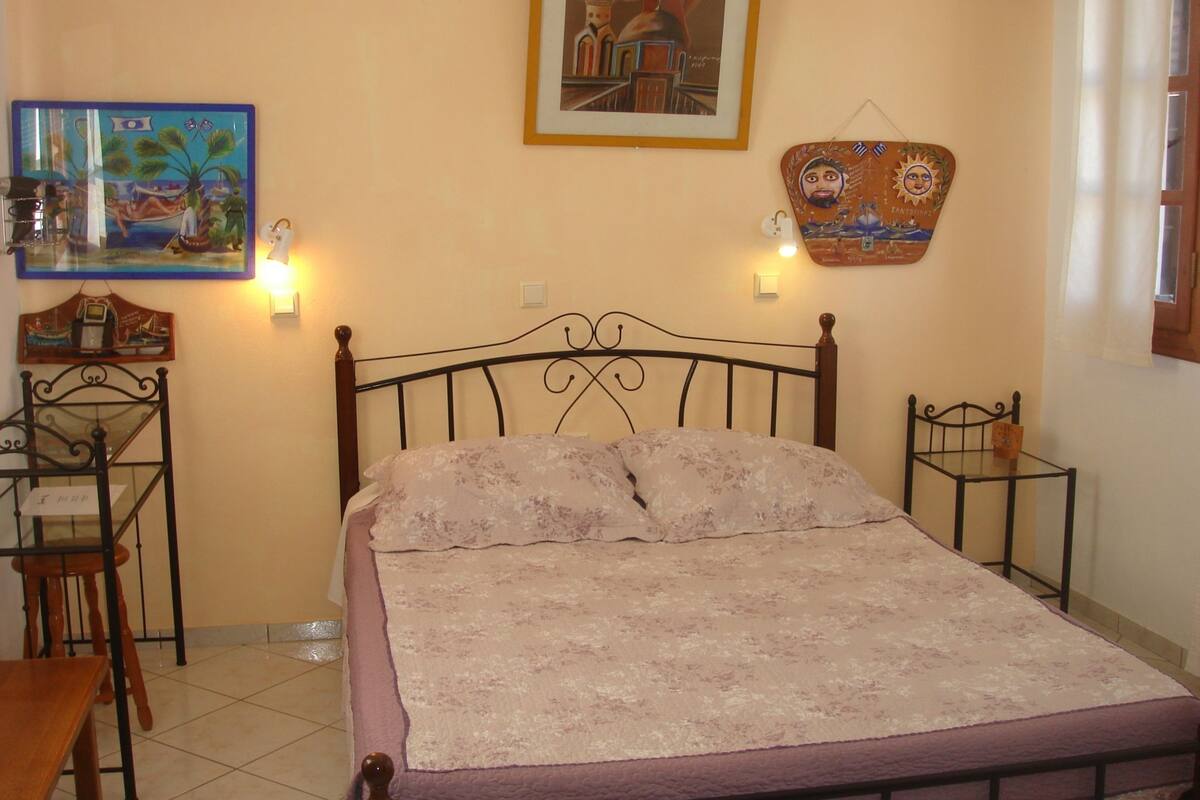 Une chambre à coucher comprenant un lit, une table de chevet, une chaise, une table et des œuvres d’art murales.