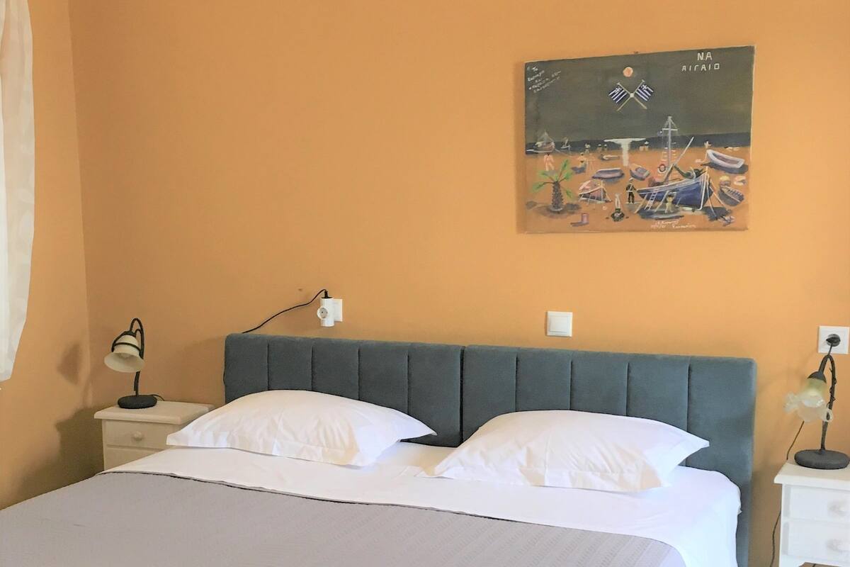 Une chambre à coucher comprenant un lit, deux tables de chevet, une commode, un tableau et un luminaire au plafond.