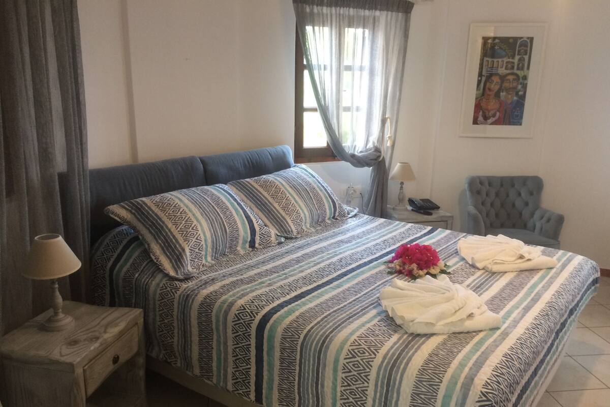 Un lit bien fait, avec une literie à motifs, une lampe de chevet, une chaise et un tableau encadré au mur.