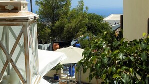 A balcony with a view of the sea, a table with a vase, and potted plants. - Argonaftes (Santorini)