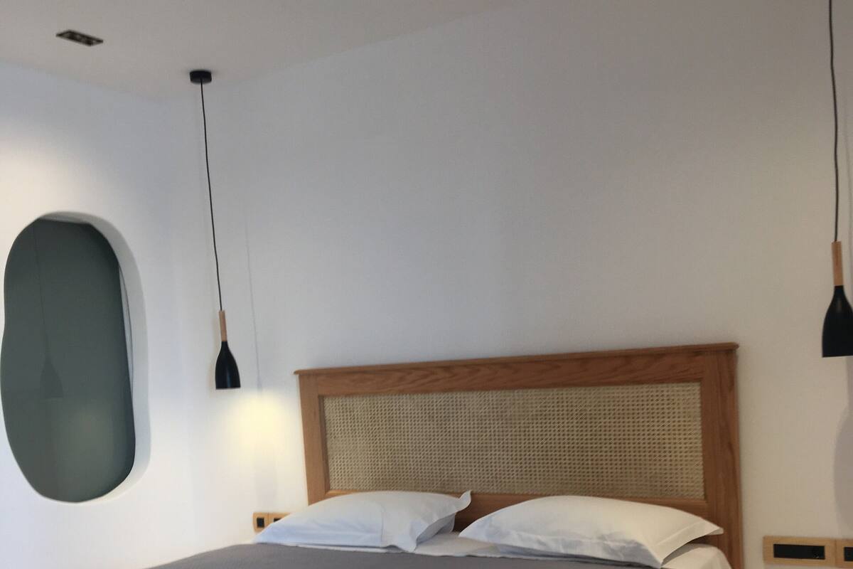Une chambre moderne avec un grand lit, une tête de lit en bois et deux lampes suspendues.