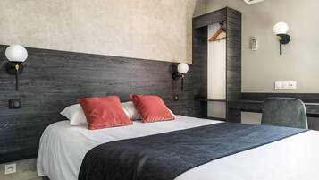 Une chambre d’hôtel moderne avec un grand lit, deux lampes fixées au mur, un bureau avec une chaise et un porte-manteau mural.