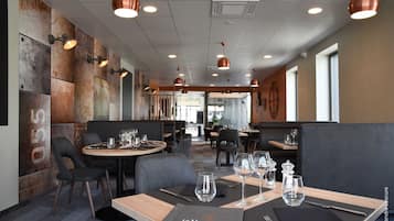 L’intérieur d’un restaurant, avec des banquettes, des tables rondes et des luminaires suspendus.