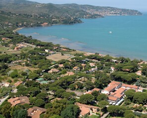 An aerial view of a coastal town with residential buildings, a marina, and a clear view of the sea.