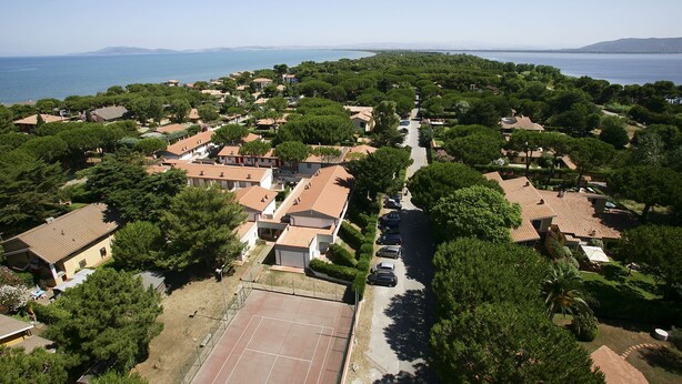 Vue aérienne d’un quartier résidentiel avec des maisons, un court de tennis et une vue sur la mer.