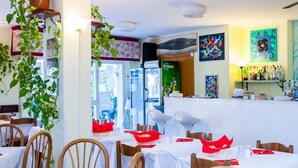 Un restaurant avec des tables dressées pour le service, un comptoir où sont exposés divers produits et une fresque murale.