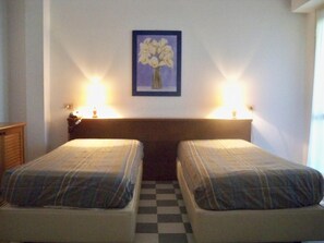 A room with two beds, a checkered floor, and a framed picture on the wall.