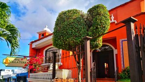 Un hotel con fachada roja, un letrero, una entrada protegida por una reja y una escalera que conduce a la puerta principal.