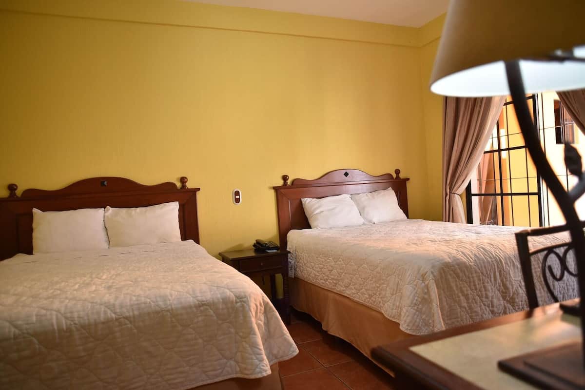 Una habitación con dos camas, cabeceros de madera, una mesita de noche y una lámpara.