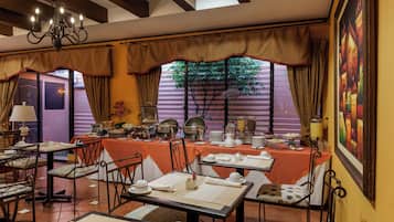 Un comedor con mesas dispuestas para el desayuno, una araña y un ventanal con cortinas.