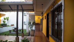 Un patio con una fuente, plantas en macetas y un sendero empedrado que lleva a una puerta con un ventanal.