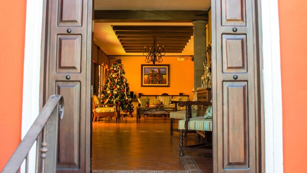 Una puerta que da a una habitación con un árbol de Navidad, una araña y una alfombra estampada.
