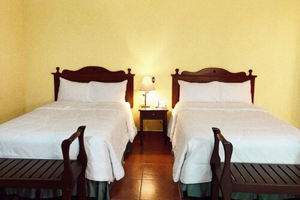 Una habitación de hotel con dos camas individuales, una mesita de noche con lámpara y una pequeña mesa con una silla.