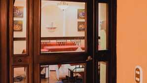 A café entrance with a sign reading "Café Terranova," a tiled floor, and a dining area visible through the glass doors. - Hotel Villa Terra (San Salvador)