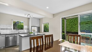 A modern kitchen with a dishwasher, a large island with chairs, and a view of a green garden through a window.