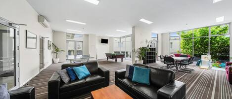 Amplio espacio interior con sofás de cuero negro, una mesa de centro de madera, mesa de billar y comedor con sillas y una mesa.