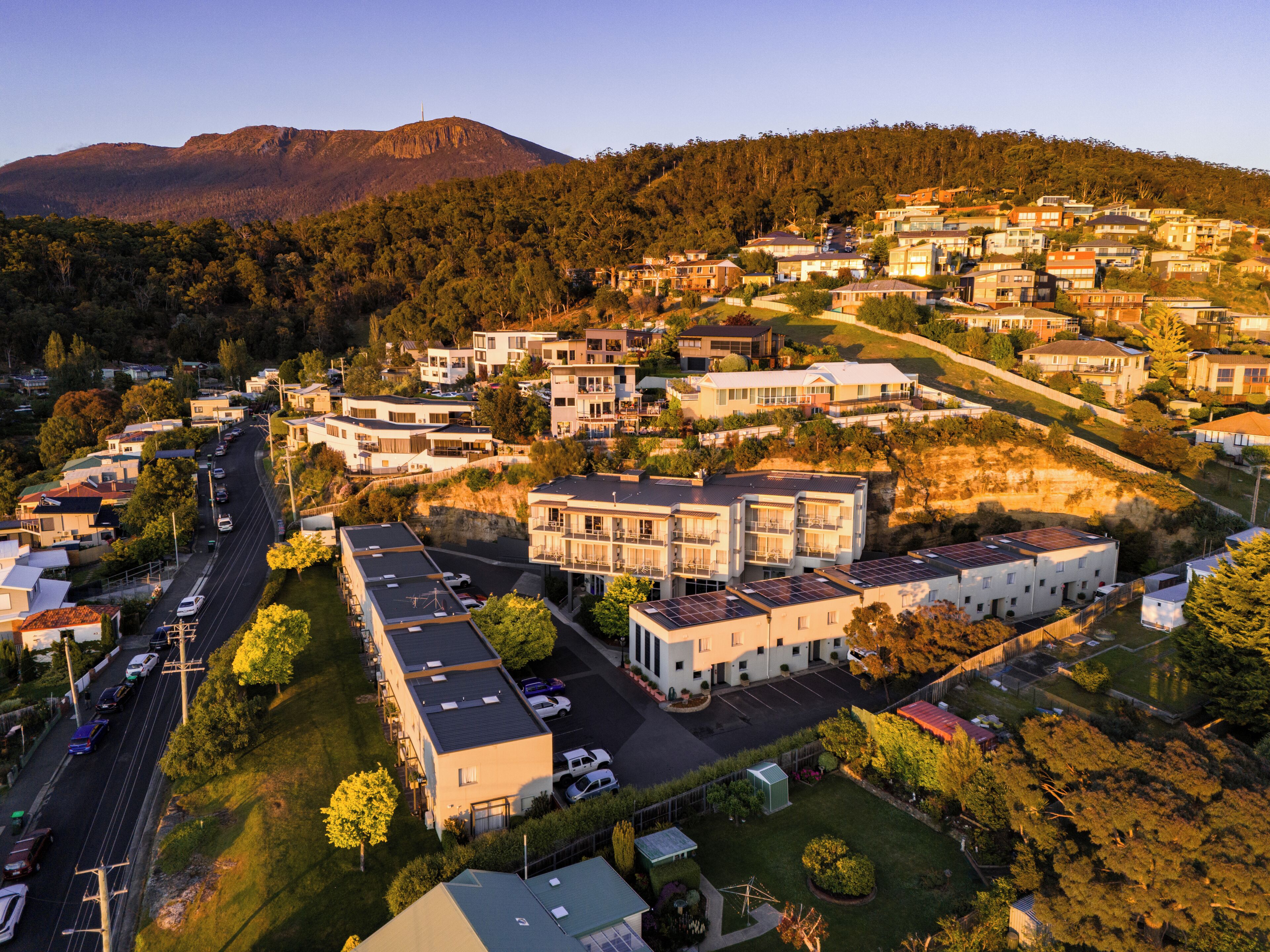 A residential area with modern houses, a main road, and a mountain in the background.