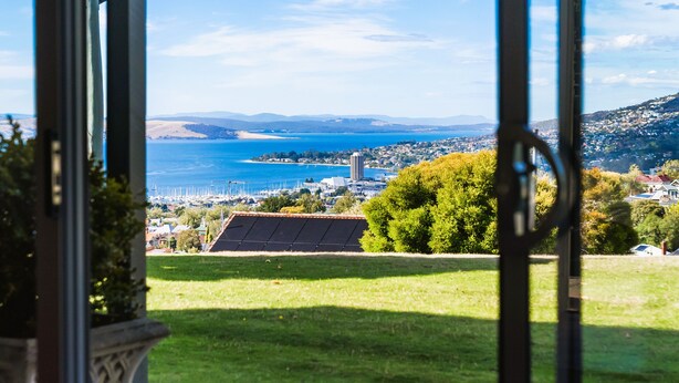 A view through a window with a solar panel, a grassy area, and a distant town by the sea.