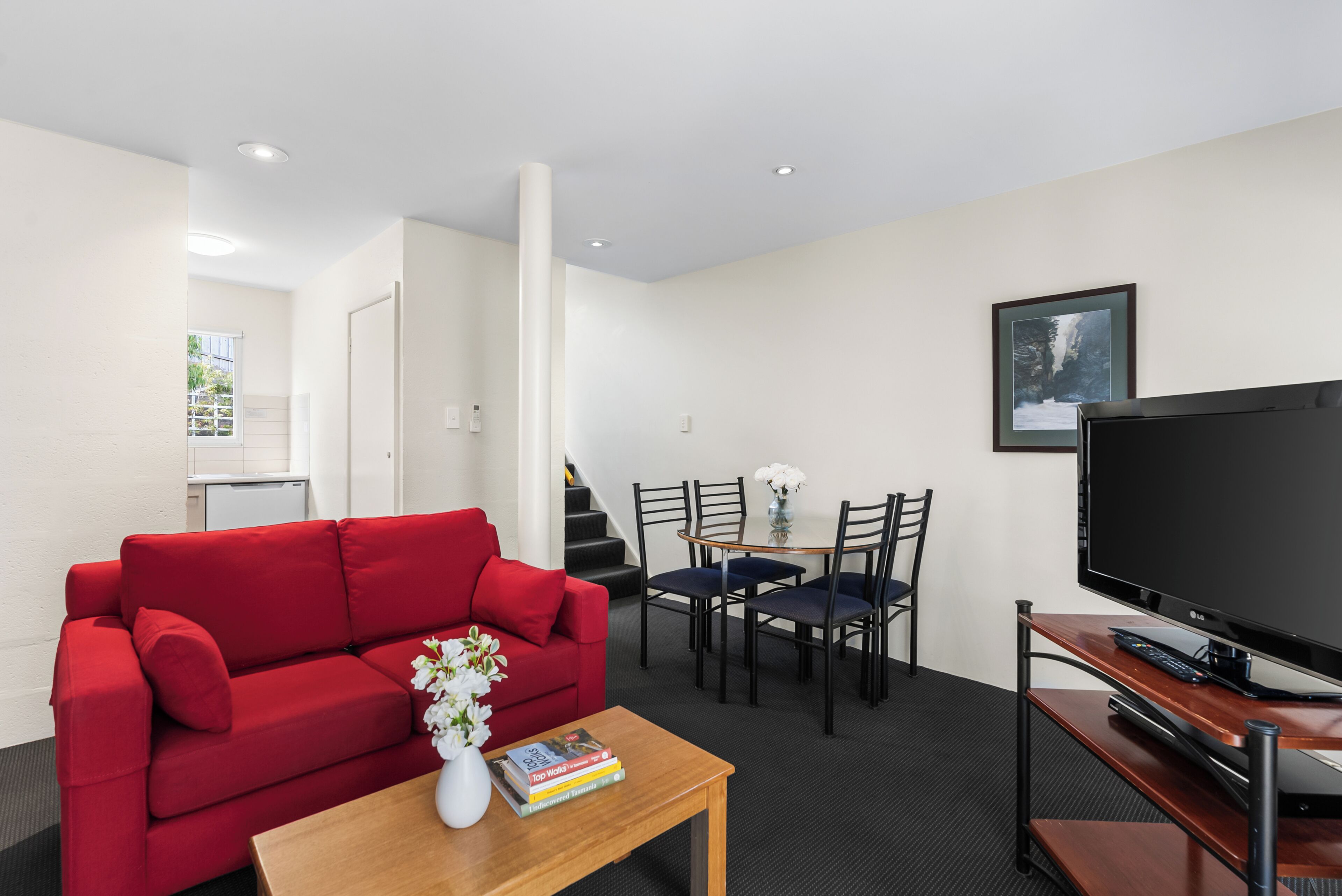 A modern living room with a red sofa, a coffee table with books, a TV, and a dining area with chairs and a table.