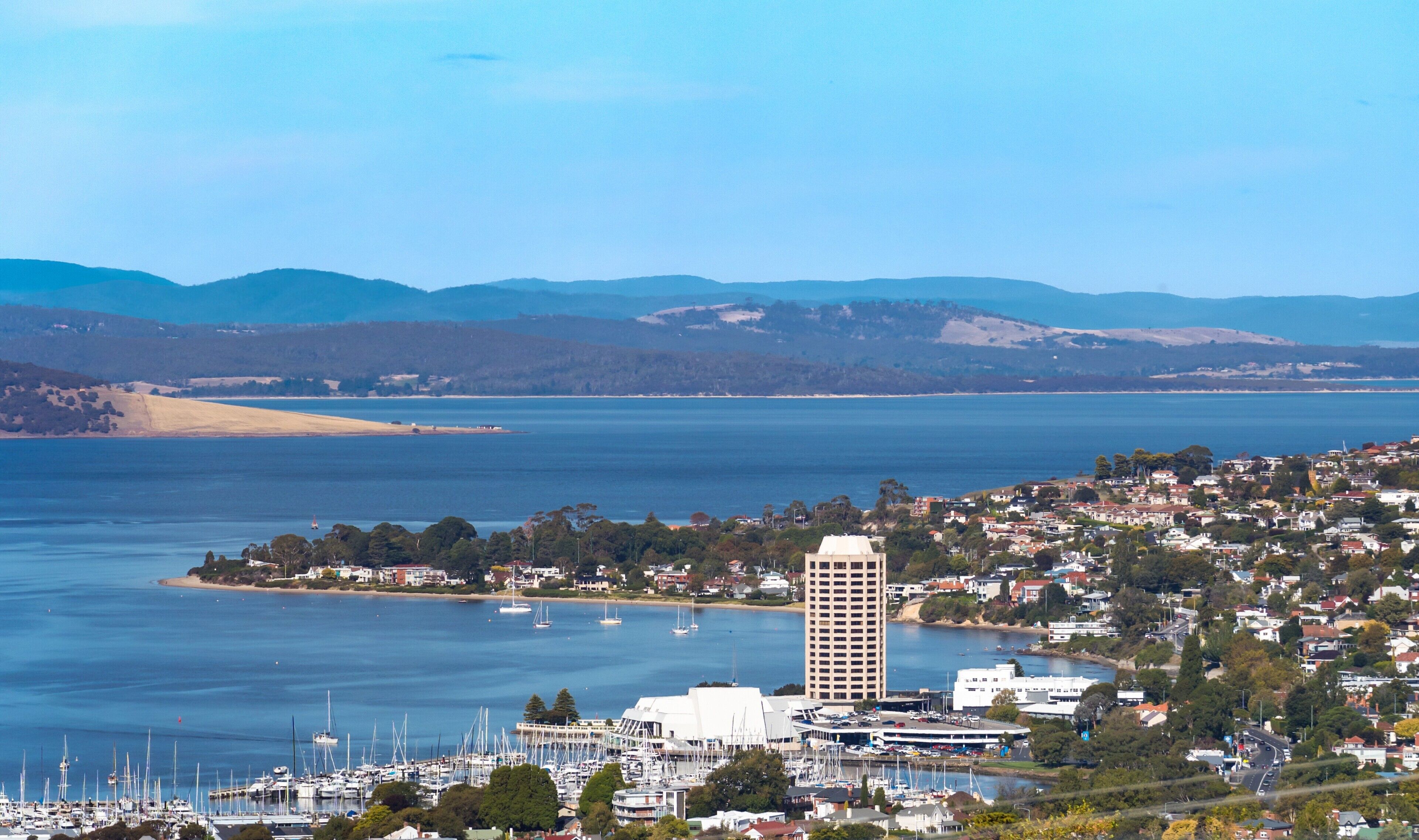 A coastal town with a marina, a prominent building, and surrounding hills.