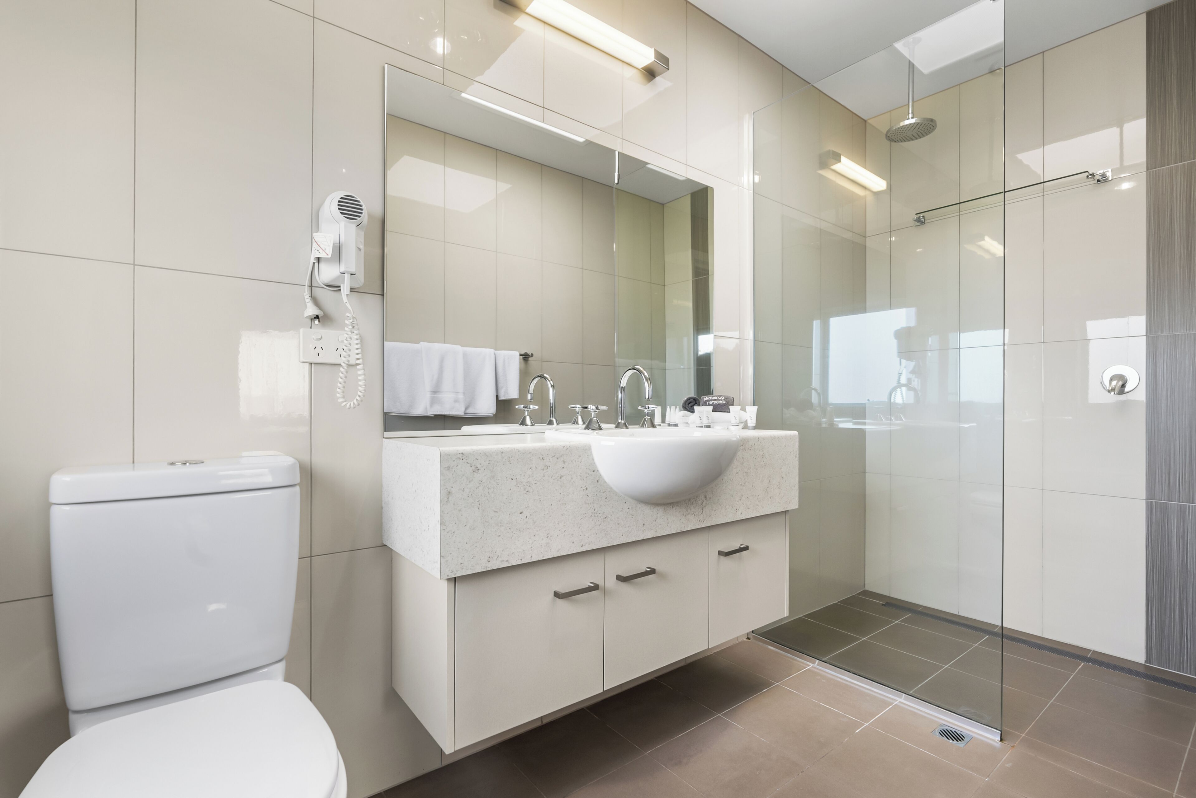 Une salle de bain moderne comprenant des toilettes, un lavabo avec un miroir et une douche à parois de verre.