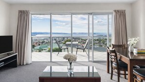 A modern hotel room with a large sliding glass door leading to a balcony with a city view.