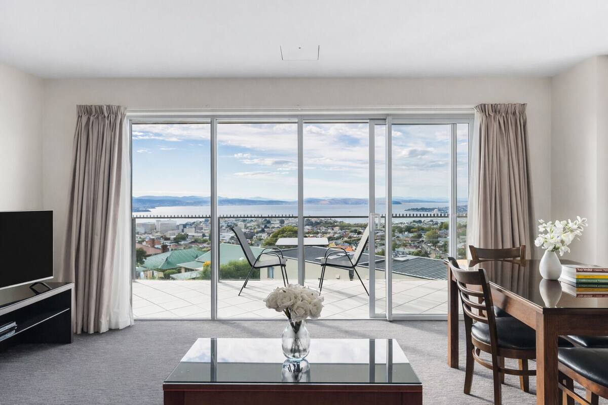 A modern hotel room with a large sliding glass door leading to a balcony with a city view.