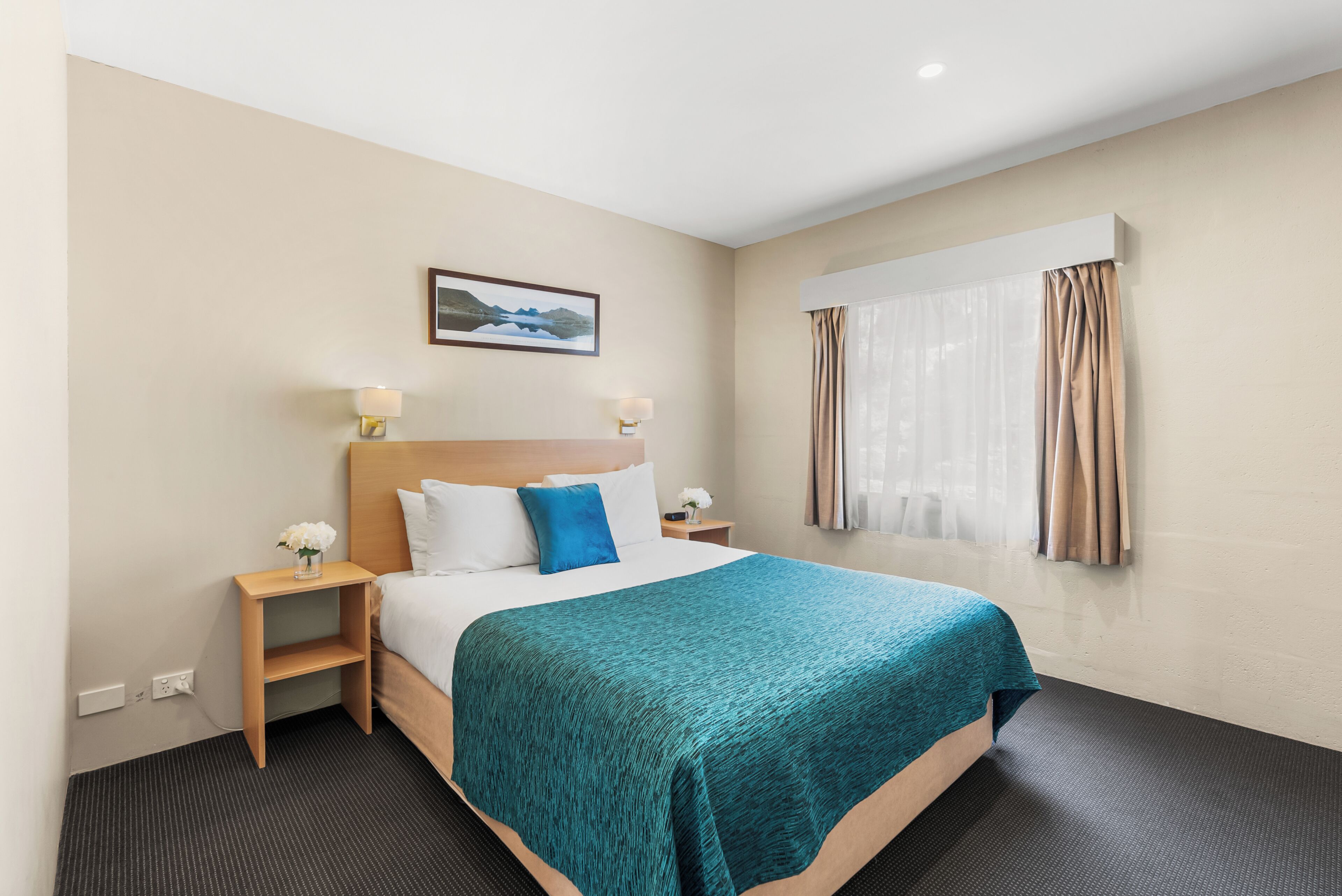 Une chambre d’hôtel avec un lit, une table de chevet, une lampe, un tableau au mur et une fenêtre avec des rideaux.