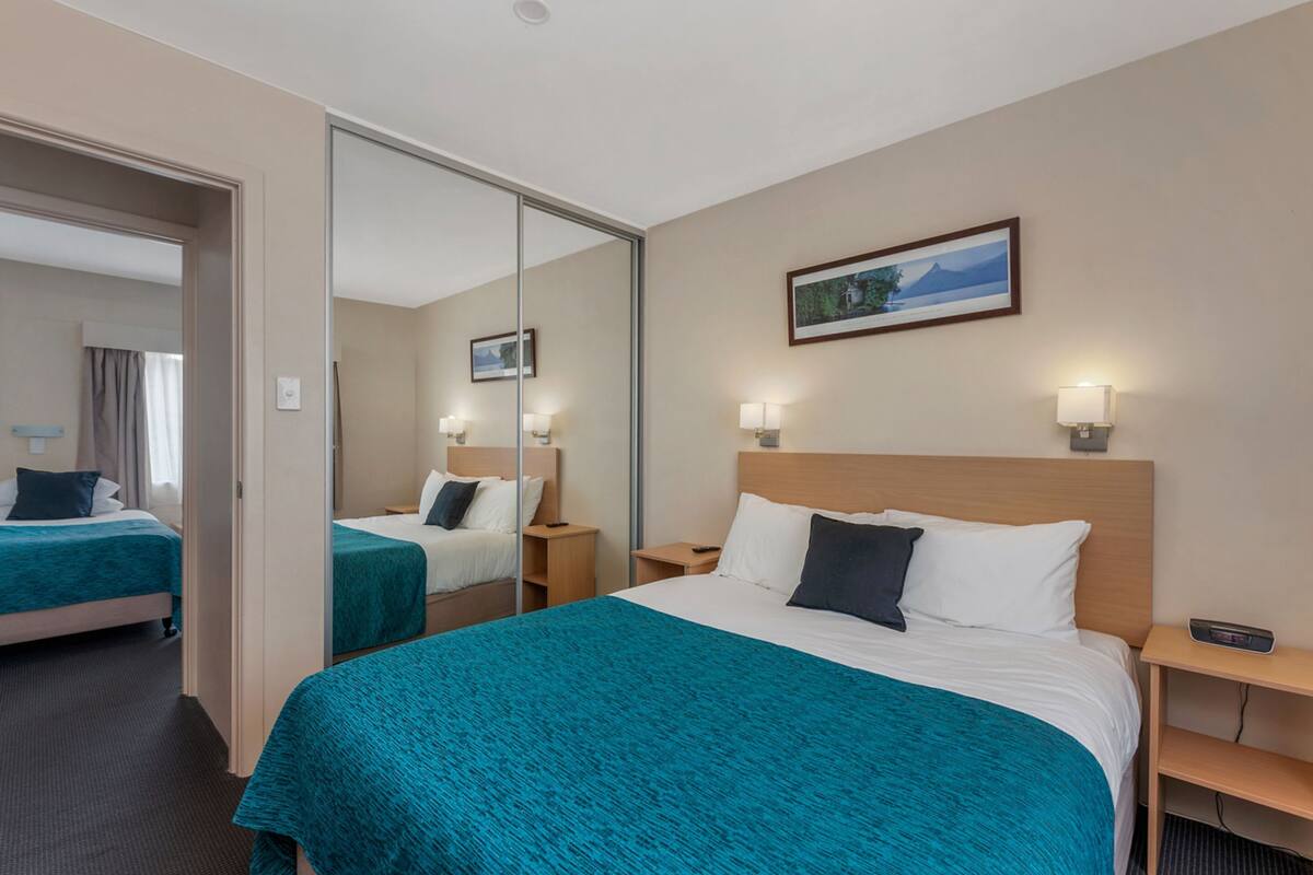 A hotel room with a large bed, a bedside table, a nightstand, a mirror, and a wall-mounted picture.