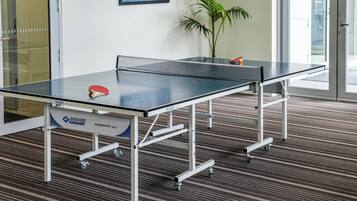 Une table de ping-pong avec un filet, une raquette rouge et une table à roulettes, le tout installé dans un espace intérieur.