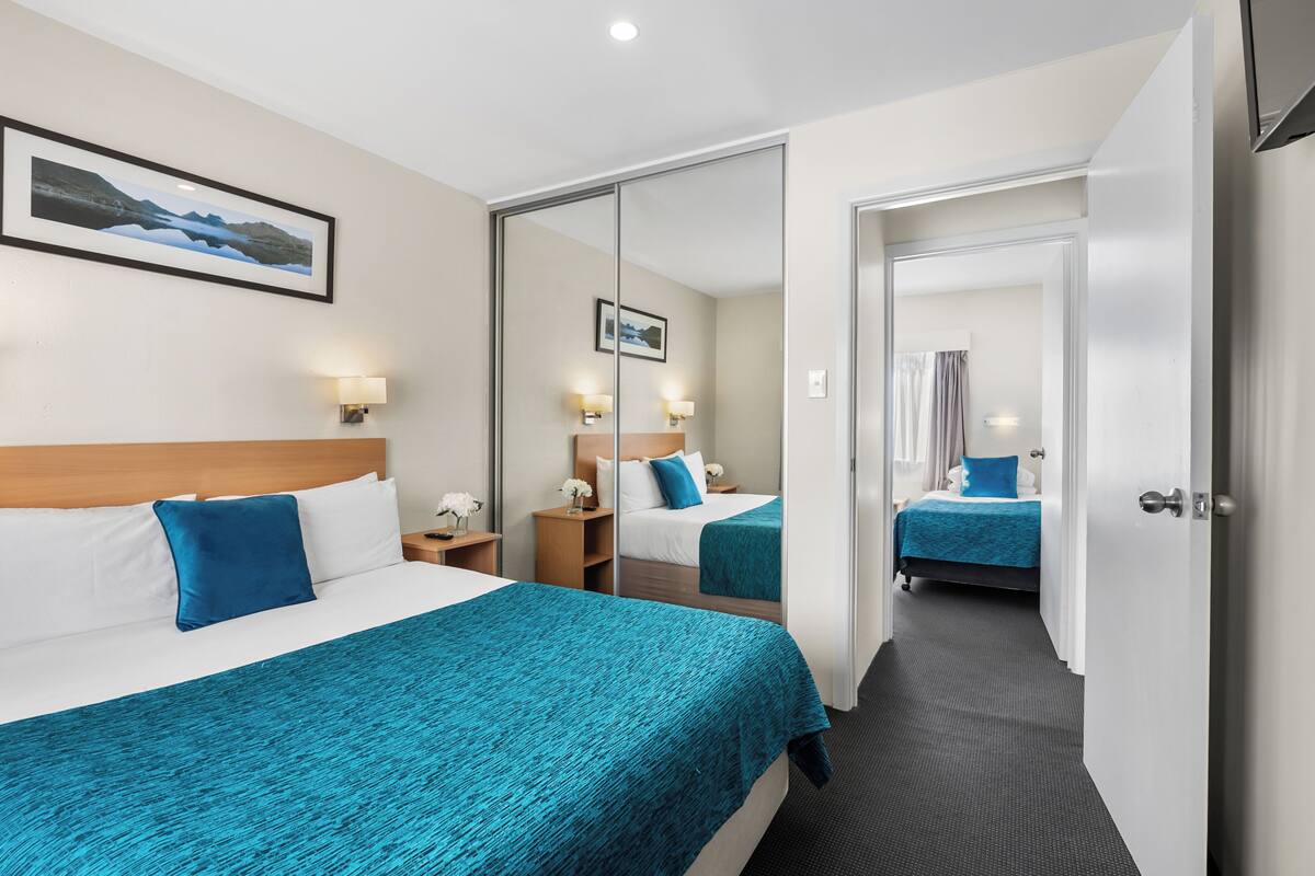 A hotel room with two beds, a large mirror, a nightstand with a lamp, and a framed picture on the wall.