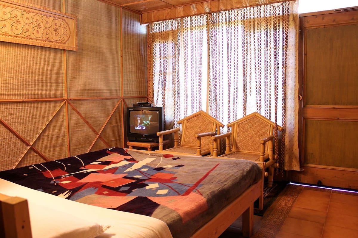 A room with a bed, a television, and two wooden chairs.