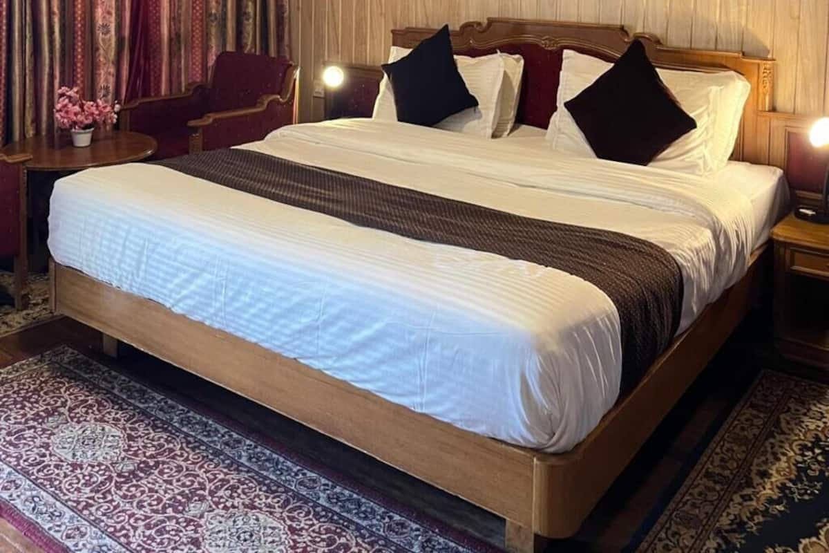A hotel room with a large bed, wooden panel walls, a patterned rug, and a nightstand with a lamp.