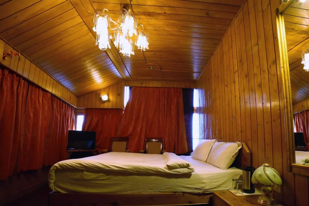 A wooden-paneled room with a bed, a television, a desk, and a lamp.