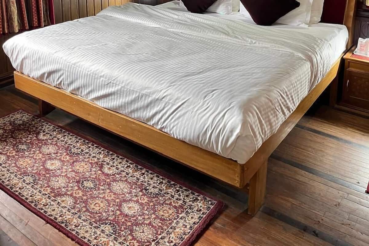 A wooden-paneled bedroom with a bed, pillows, a rug, and two wall-mounted lights.