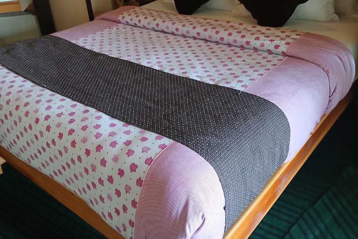 A neatly made bed with patterned bedding, a wooden headboard, and a dark curtain backdrop.