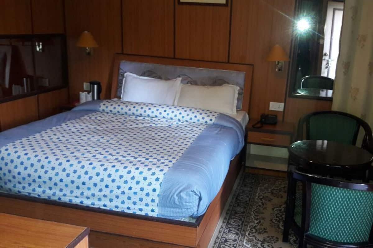 A hotel room with a bed, a small table, a chair, a lamp, and a mirror.
