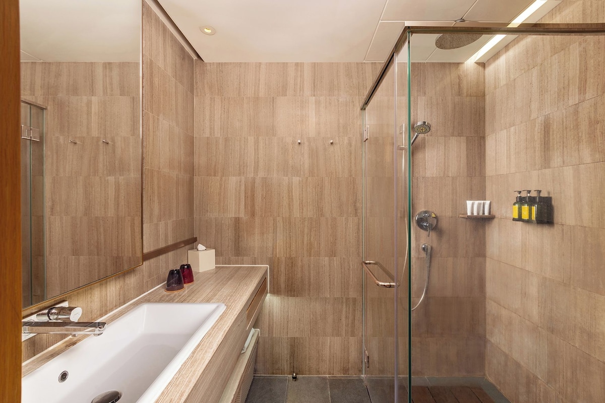 A modern bathroom with a glass-enclosed shower, a large mirror, and a wooden vanity with a white sink.