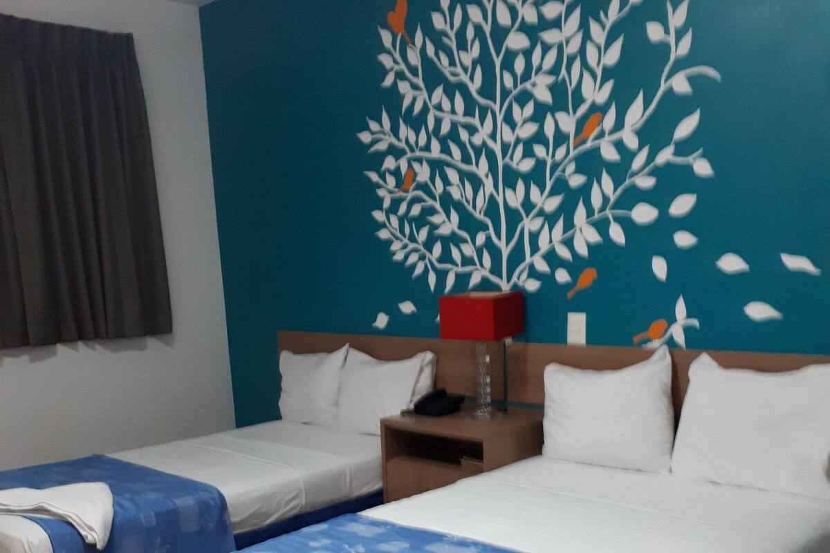 Une chambre d’hôtel avec deux lits, une table de chevet, une lampe rouge et une fresque murale.