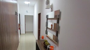 Un pasillo con una puerta de madera, un banco con un frutero y un estante en la pared con un espejo y objetos decorativos.