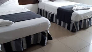Una habitación de hotel con dos camas individuales, cada una con cubrecama a rayas y un cabecero, y un almohadón blanco.