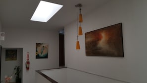 En hall med en taklampa, en tavla, en brandsläckare och en stor, abstrakt målning på väggen.