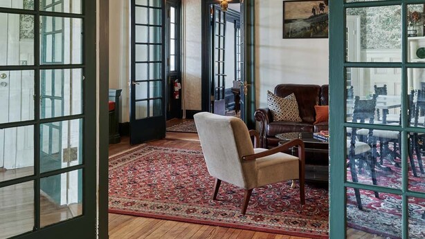 A spacious room with a large wooden floor, a patterned rug, a sofa, and a dining table with chairs. - The Dewey (Lenox)