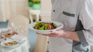 Una persona con delantal blanco sostiene un plato de ensalada.