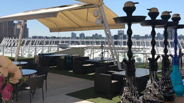 Terraza al aire libre con mesas, sillas, un dosel y jarrones decorativos.