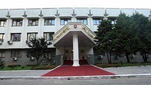 Un edificio con una entrada central, flanqueada por dos columnas, y una alfombra roja que conduce a la entrada.